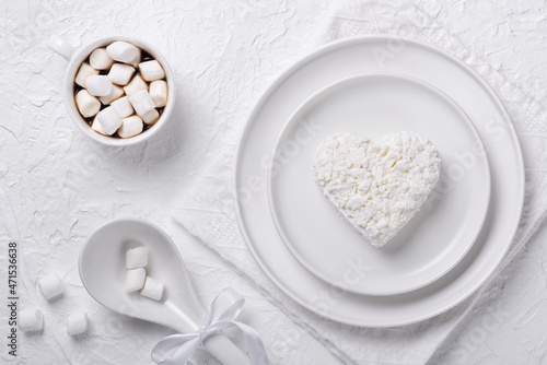 Heart shaped cottage cheese in a plate, coffee and marshmallows on a white table
