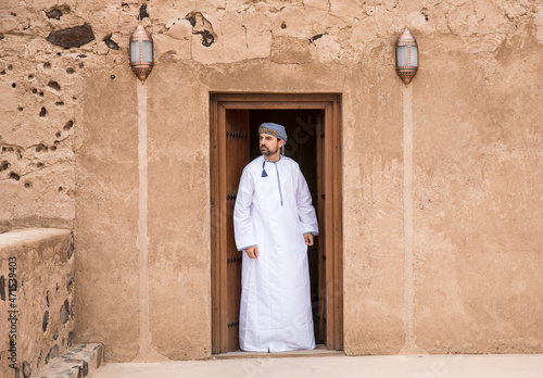 omani man in traditional outfit at a doorway of an old house