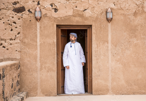 omani man in traditional outfit at a doorway of an old house photo