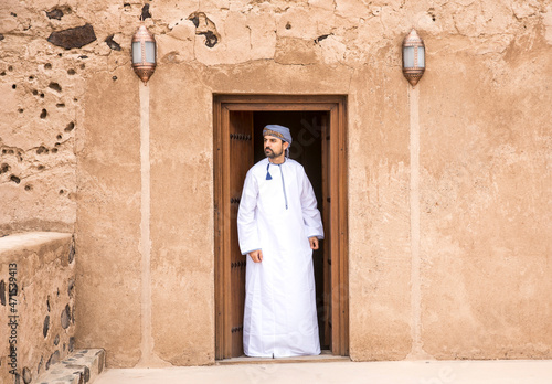 omani man in traditional outfit at a doorway of an old house