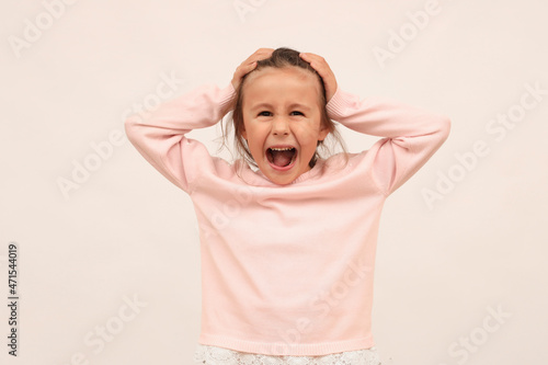 Foto An angry little girl loses her temper holding her head, argues, complains, looks angry and dissatisfied, screams in rage, stands on a white background