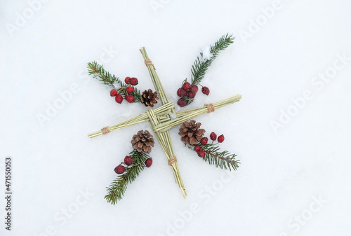 Brigid's cross and fir branches and berries on snow. symbol of Imbolc sabbat. ireland handmade amulet made from straw. Wiccan tradition for blessed and protected house. flat lay