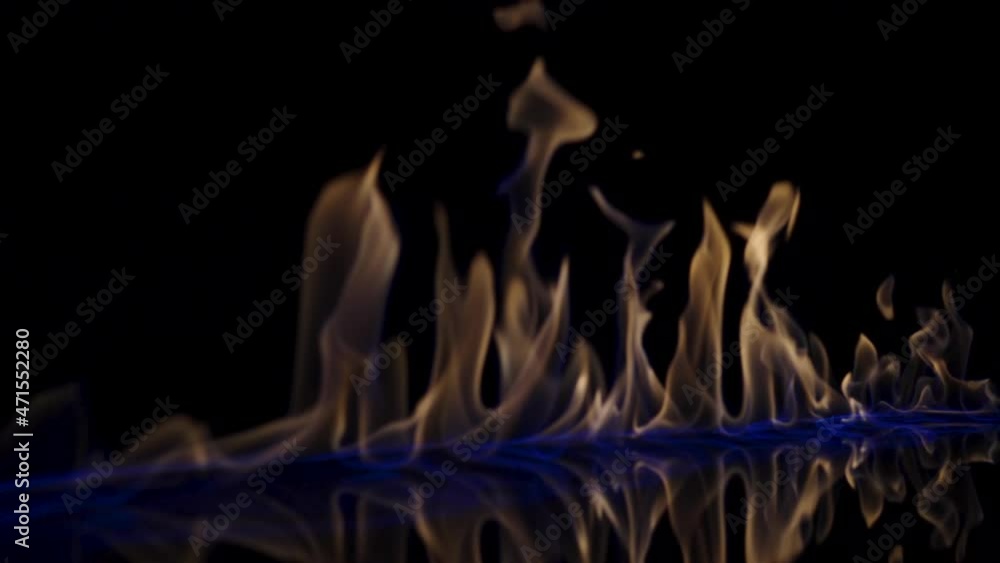 Flammable liquid or petrol stains on black reflective background flash and ignite. An explosion of fire, flaming tongues burning in blue light close up, slow motion. Blaze flames, setting fire to gas. Flammable liquid or petrol stains on black reflective background flash and ignite. An explosion of fire, flaming tongues burning in blue light close up, slow motion. Blaze flames, setting fire to gas.