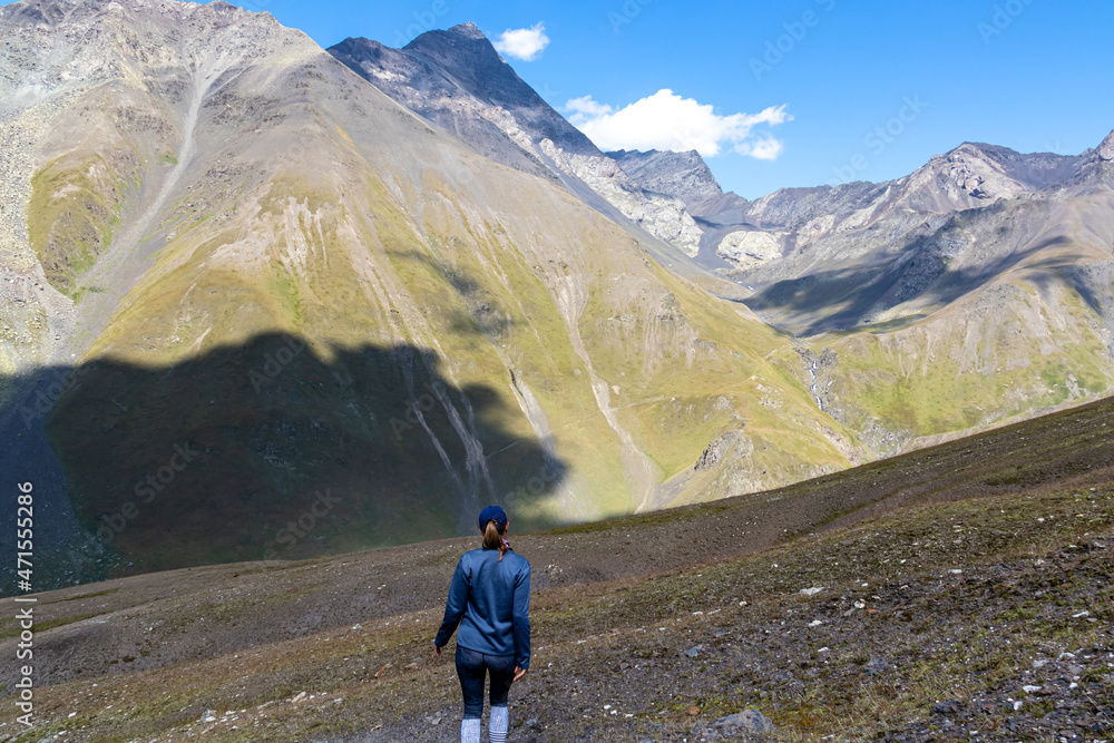 A woman watching the sharp mountain peaks of the Chaukhi massif form the Chaukhi Pass in the Greater Caucasus Mountain Range in Georgia, Kazbegi Region. The female backpacker enjoys the calmness. Hike