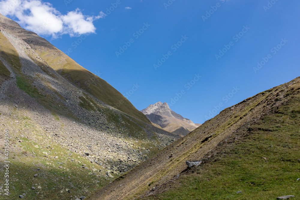 A panoramic view on the green hills and sharp ridges of the mountain peaks of the Chaukhi massif in the Greater Caucasus Mountain Range in Georgia, Kazbegi Region. Wanderlust. Clear Sky. Hike
