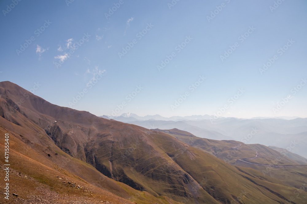 Panoramic view the a valley near the village of Roshka n the Greater Caucasus Mountain Range in Georgia,Kazbegi Region. A mountain road is leading over the green hills connecting the village. Remote