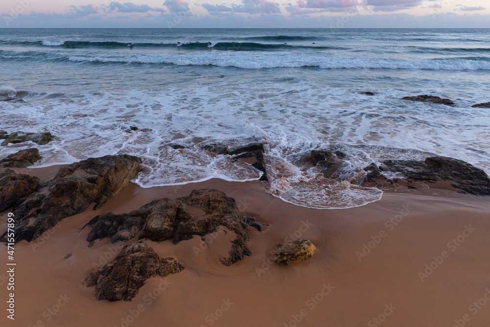 Fototapeta premium Carcavelos Beach after sunset. The last surfers in the ocean. Portugal.