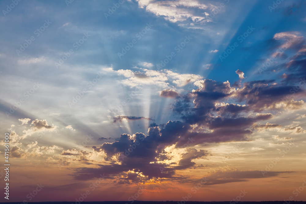 Dramatic colorful sky background with rays of rising sun through clouds