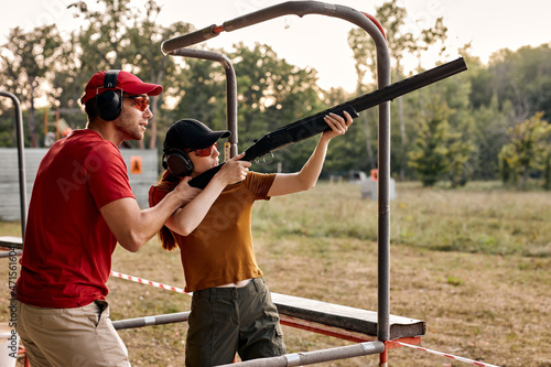 young man and woman in goggles and headset preparing to shoot, ready to shoot. Skilled experienced man is teaching female in outdoor range. Firearms for sports shooting, hobby. Side view.