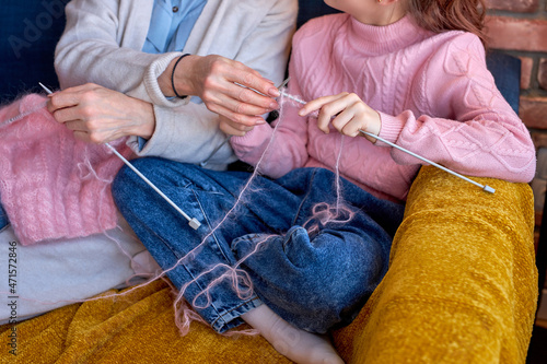cropped caucasian elderly woman teaching daughter to knit at home in living room. retired grandmother spends time together with teenage girl, at home. leisure, activity, hobby concept