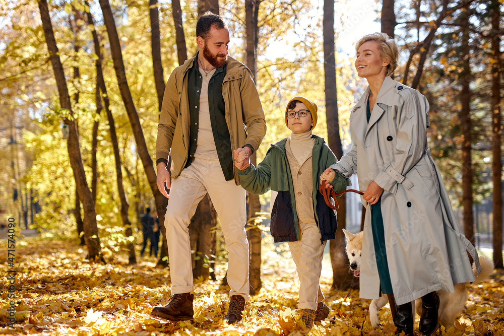 Family, weekends and people concept. parents and child walking with dog in warm autumn day in park. beautiful pleasant caucasian family have rest, enjoying warm weather during leaf fall