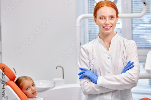 Confident Dentist Orthodontist Posing At Camera At Work Place In Clinic Hospital  Smiling  Looking Positive And Endearing  Attractive. People  Medicine  Healthcare  Stomatology. Patient in Background