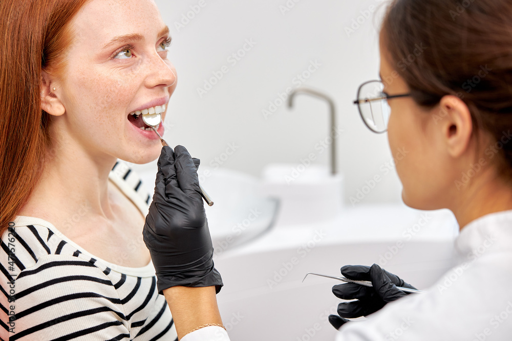 Happy redhead woman is being examined by dentist at modern dental clinic. Healthy teeth and medicine, stomatology concept. Cropped female Professional dentist using speacial tools at work Happy redhead woman is being examined by dentist at modern dental clinic. Healthy teeth and medicine, stomatology concept. Cropped female Professional dentist using speacial tools at work