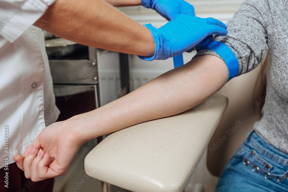 Female medical employee hands hold tube and needle during drawing blood from man arm.