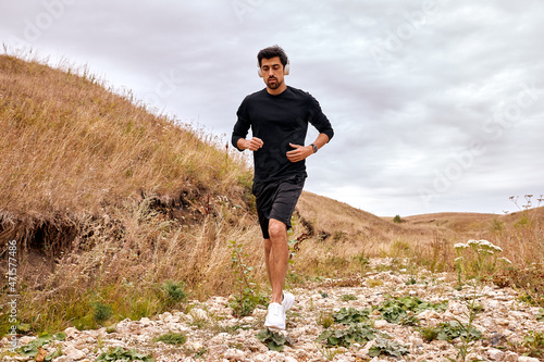 Strong and fit caucasian sportsman is running forward across the stones in mountains at summer morning, alone. Active workout on fresh air before marathon. Recreation, healthy lifestyle, sport