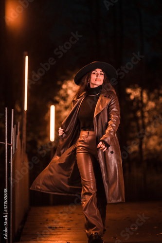 Pretty Caucasian girl with hat walking at night in a park. Winter fashion and lifestyle at night, vertical photo