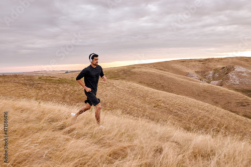 Well-built male running in rural urban field in countryside alone, fitness concept. bearded guy outdoors on fresh air, concentratded on training, active workout. in mountains before sunrise