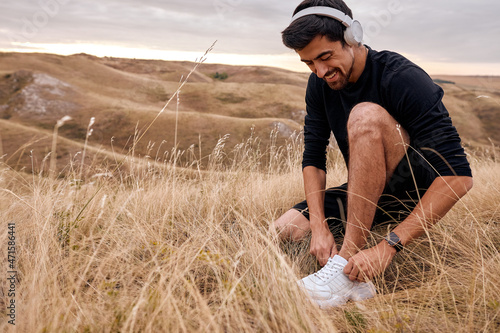 Photos Smiling Male Tying Laces On Sneakers Preparing For Jogging Running, Wearing Headphones, During Sunrise In The Morning