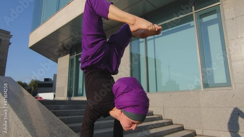 Pincha Mayurasana balance outdoors. Moving footage muslim girl wearing hijab islamic female yogi woman doing handstand yoga acrobatic exercise arm muscles holds weight on forearms and legs in air photo