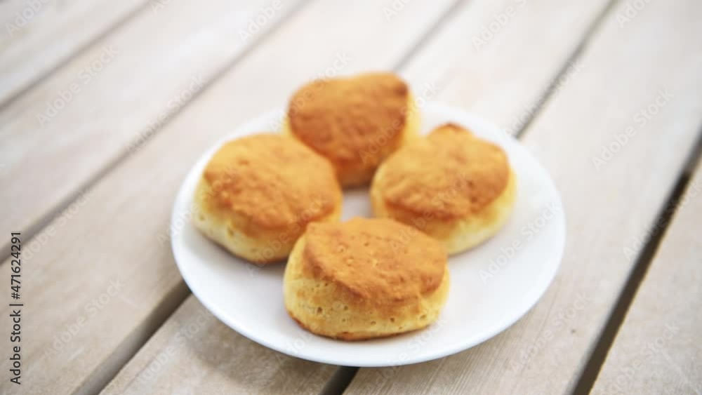 Rack focus macro closeup on four buttermilk breakfast biscuits on white plate at kitchen wooden table Rack focus macro closeup on four buttermilk breakfast biscuits on white plate at kitchen wooden table