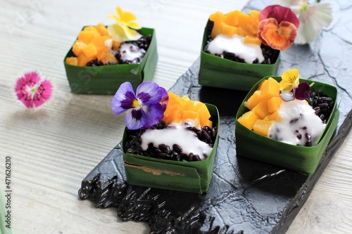 Homemade Coconut Black Sticky Rice with Mango in Pandan Leaves Cup, Selective Focus with Pansies Edibel Flower Topping photo