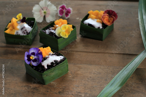 Homemade Coconut Black Sticky Rice with Mango in Pandan Leaves Cup, Selective Focus with Pansies Edibel Flower Topping photo