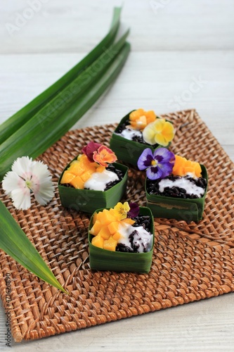 Homemade Coconut Black Sticky Rice with Mango in Pandan Leaves Cup, Selective Focus with Pansies Edibel Flower Topping photo