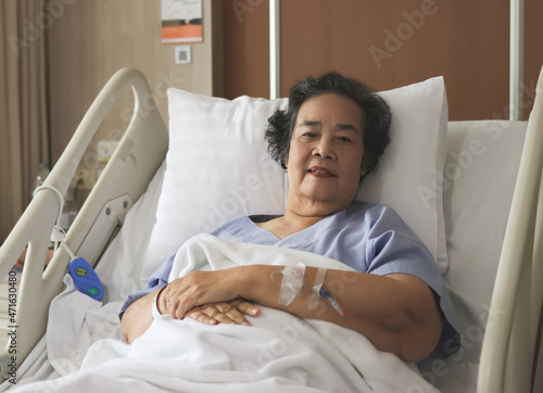 Asian senior female patient lying down in hospital bed, looking at camera. Elderly health concept.