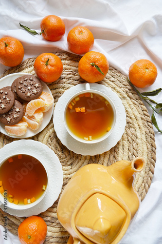 Two cups of tea, teapot, mandarins, chocolate cookies on the white bedsheet. Couple winter morning. Tea breakfast service. Cozy, warm atmosphere.