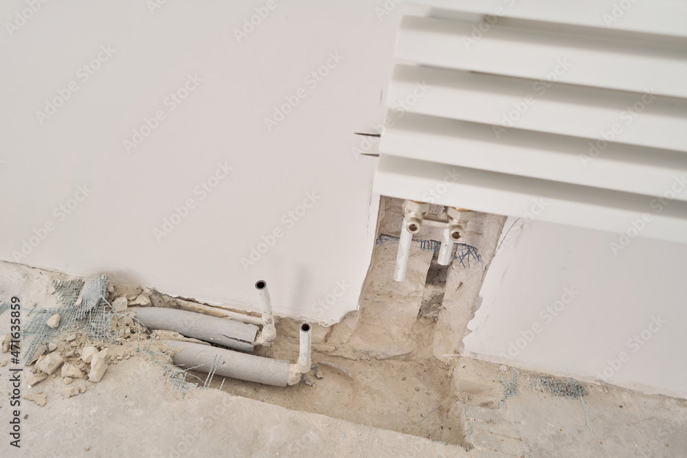 connection heating pipes to white Radiator in a new apartment under construction. Work As A Plumber, mounting water heating radiator on the white wall indoors connection heating pipes to white Radiator in a new apartment under construction. Work As A Plumber, mounting water heating radiator on the white wall indoors