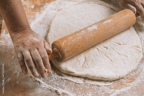 Chef is rolling the dough with the rolling pin on the on the table. Hands close-up.Cooking pasta, bread,spaghetti,khachapuri, food concept