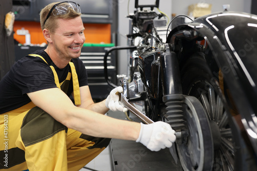 Smiling locksmith with wrench near motorcycle wheel in car workshop © megaflopp