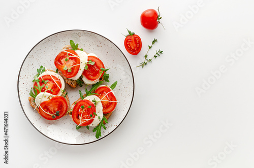 Italian food concept. Open sandwiches with mozzarella, tomatoes and arugula on white plate. Copy space. Flat lay