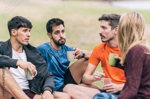 Friends drinking tea and chat with relaxed expression sitting on a park