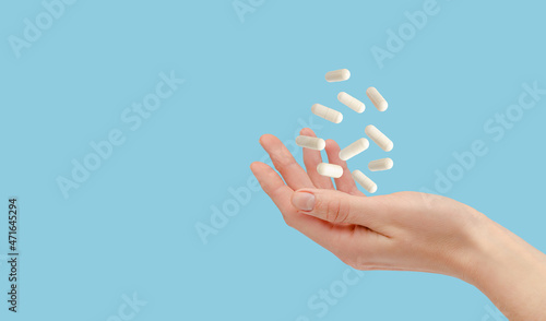 Fotografía White pills floating over female hand isolated on blue