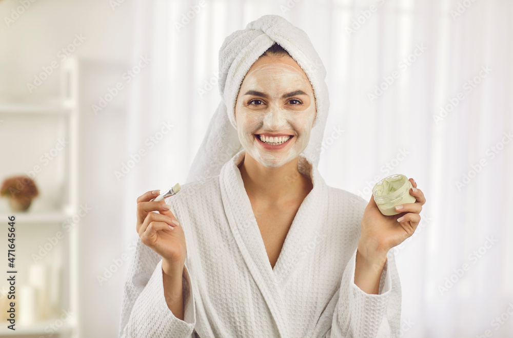 Portrait of happy young woman in bathrobe apply moisturizing face cream for healthy glowing skin. Smiling female use facial mask do morning beauty procedures. Cosmetology, skincare concept. Portrait of happy young woman in bathrobe apply moisturizing face cream for healthy glowing skin. Smiling female use facial mask do morning beauty procedures. Cosmetology, skincare concept.