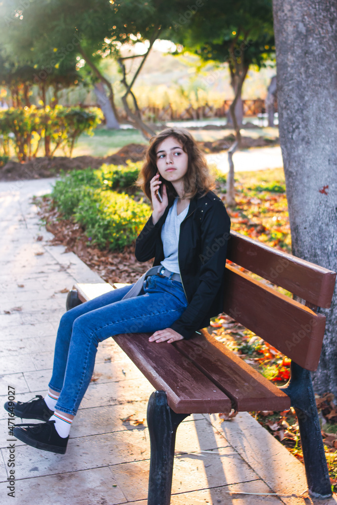 Teenager girl taking by phone on the bench in autumn park Teenager girl taking by phone on the bench in autumn park