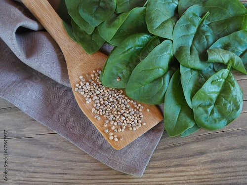 Seeds in a wooden spoon and fresh young spinach leaves with a napkin on a wooden table, flat layout. Spinacia leaf salad with vitamins for dietary nutrition. Farming and gardening