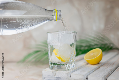 water or tonic is poured from a bottle into a glass with ice and lemon