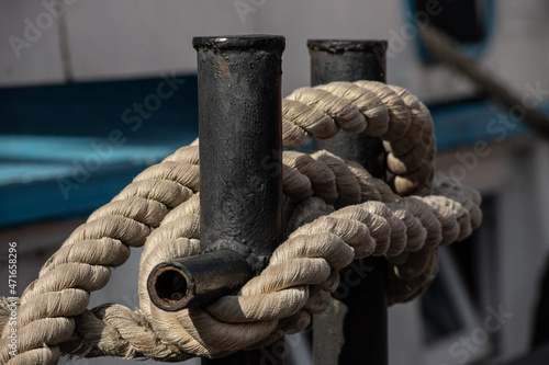 Worn old rusty mooring bollard with heavy ropes on the deck of a ship, closeup