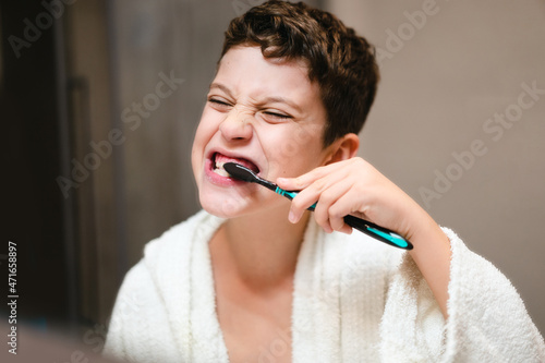 Little boy in bathrobe washing teeth in front of the mirror