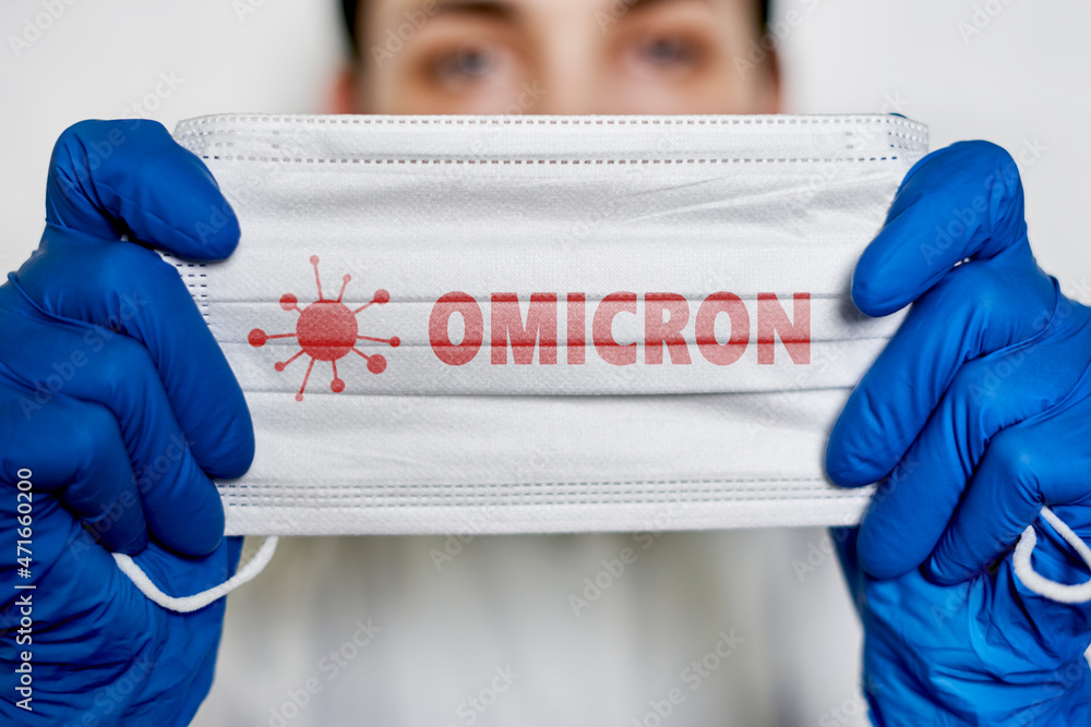 Female doctor holds a face mask with - Omicron variant text on it. Covid-19 new variant - Omicron. Omicron variant of coronavirus. SARS-CoV-2 variant of concern - obrazy, fototapety, plakaty 