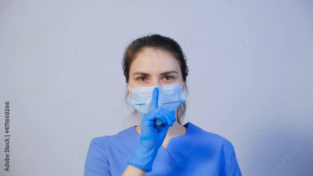 A doctor in a medical mask holds a finger in front of his mouth, a gesture of silence or secretion. A doctor in a medical mask holds a finger in front of his mouth, a gesture of silence or secretion.