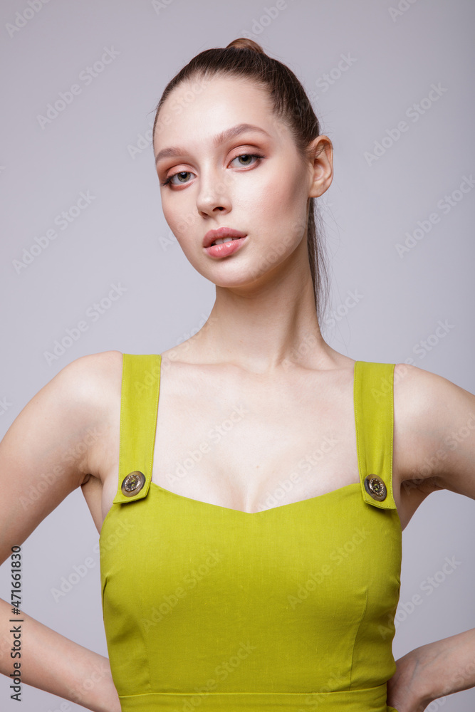 High fashion photo of a beautiful elegant young woman in a pretty yellow sage gold dress, high-heeled shoes, hair pulled back in a ponytail posing over white, soft gray background. Studio Shot. High fashion photo of a beautiful elegant young woman in a pretty yellow sage gold dress, high-heeled shoes, hair pulled back in a ponytail posing over white, soft gray background. Studio Shot.