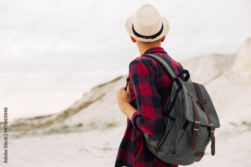 Male hipster traveler with backpack in hat looking forward to amazing mountains and valleys view