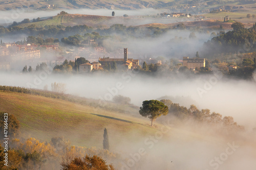 Asciano, Siena. Paesaggio con il borgo nella nebbia all' alba 