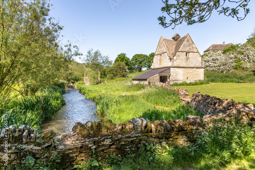 The old stone dovecote (c.1600 AD) beside the infant River Windrush as it flows through the Cotswold village of Naunton, Gloucestershire UK photo