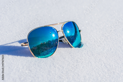 Sunglasses with blue lenses in which the forest is reflected lie on the snow
