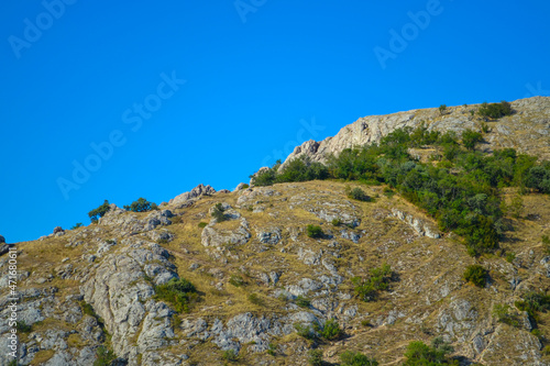 Path along the mountain to the top among bushes and stones against the blue sky in a hot southern country