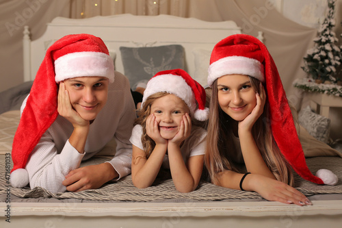 a young family with a little daughter in Santa Claus hats are lying on the bed at home Christmas